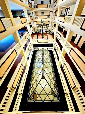 A multi-level atrium with a central glass elevator shaft, white railings, and a seating area with tables and chairs. - Royal Peninsula Hotel Chiang Mai (Chiang Mai)