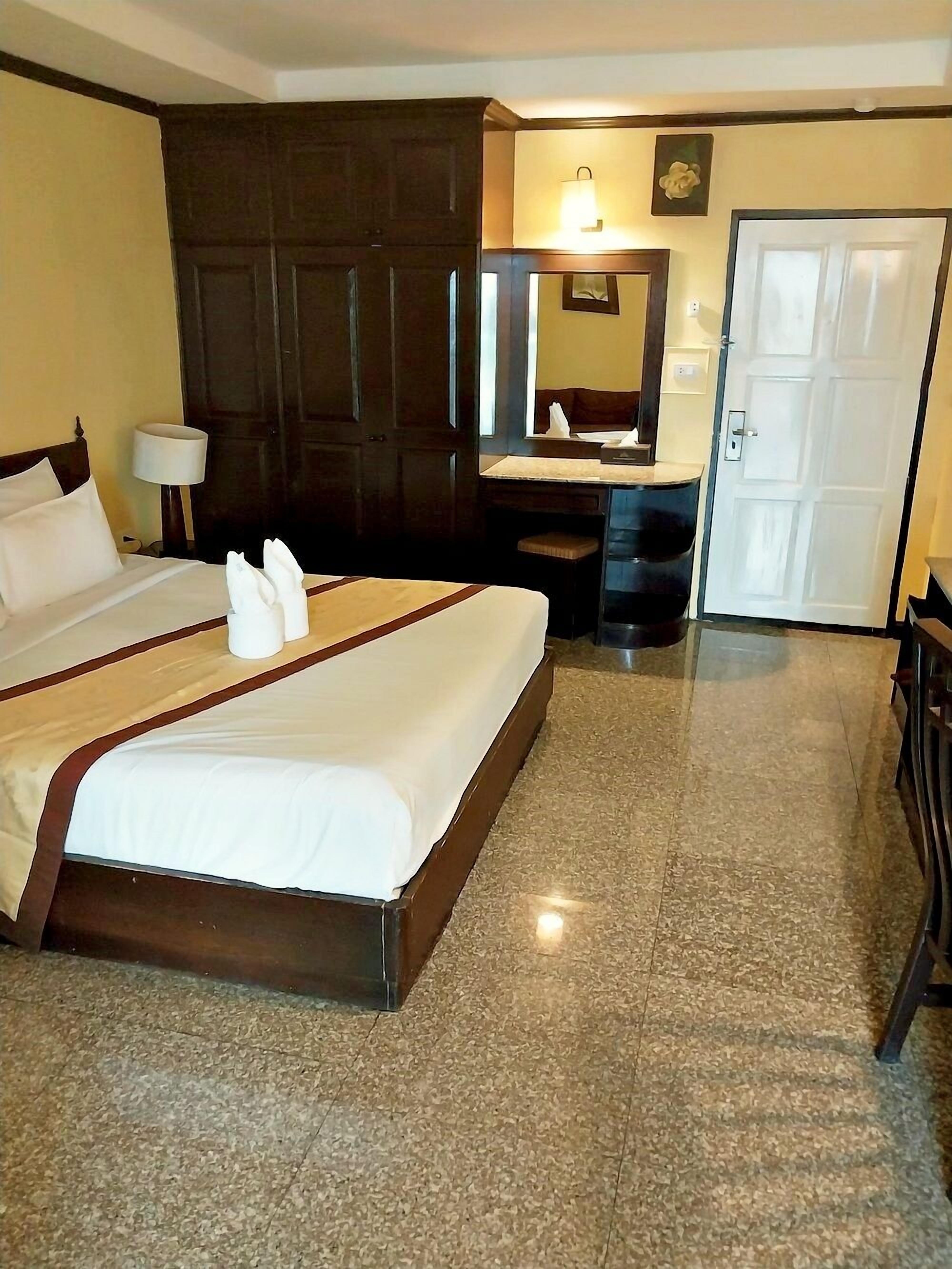 A hotel room with a large bed, a desk, a chair, a mirror, and a door.