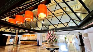 A spacious lobby with a high ceiling, a reception desk, and a decorative vase with flowers.