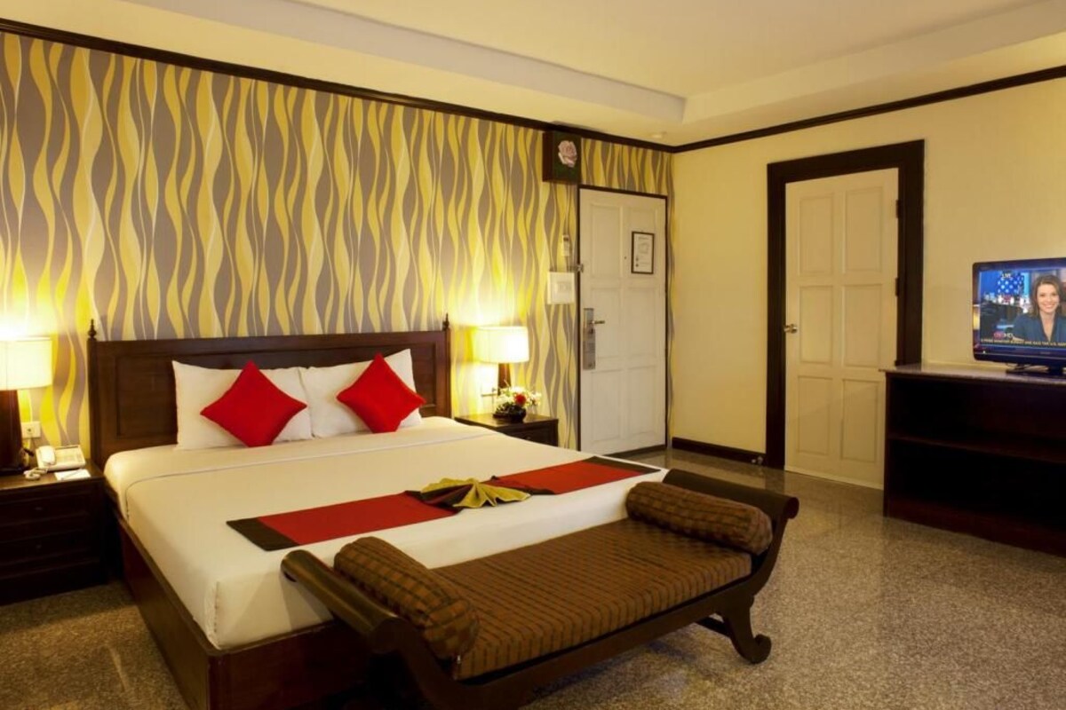 A hotel room with a large bed, a bench, a TV, and a patterned wall.