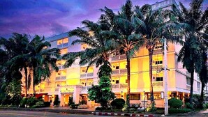 A multi-story hotel with a central atrium, surrounded by palm trees and a well-lit facade.