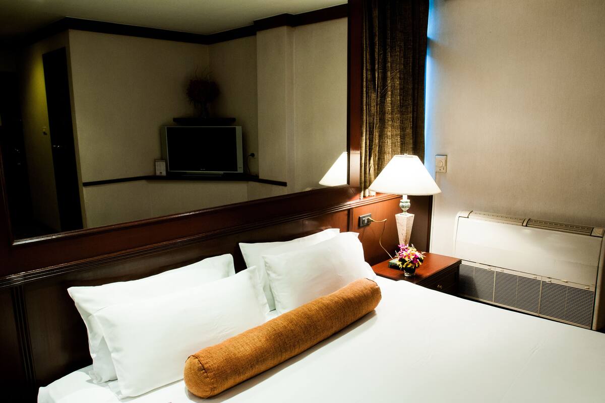 A hotel room with a neatly made bed, a bedside lamp, a TV mounted on the wall, and a window with curtains.