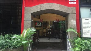 L’entrée de l’hôtel City Lodge se distingue par sa façade rouge, son logo en forme de papillon et une enseigne indiquant les services proposés, tels que le Wi-Fi gratuit, des chambres propres et une sécurité disponible 24 heures sur 24.