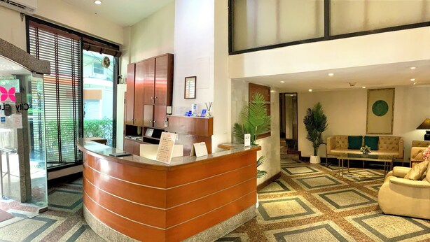 Un hall d’hôtel avec un comptoir d’accueil marron, un espace d’attente doté d’un canapé et de fauteuils, et un sol à motifs.