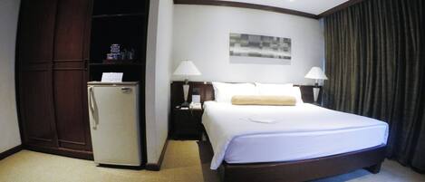 Una habitación de hotel con cama, escritorio, lámpara, armario y refrigerador.