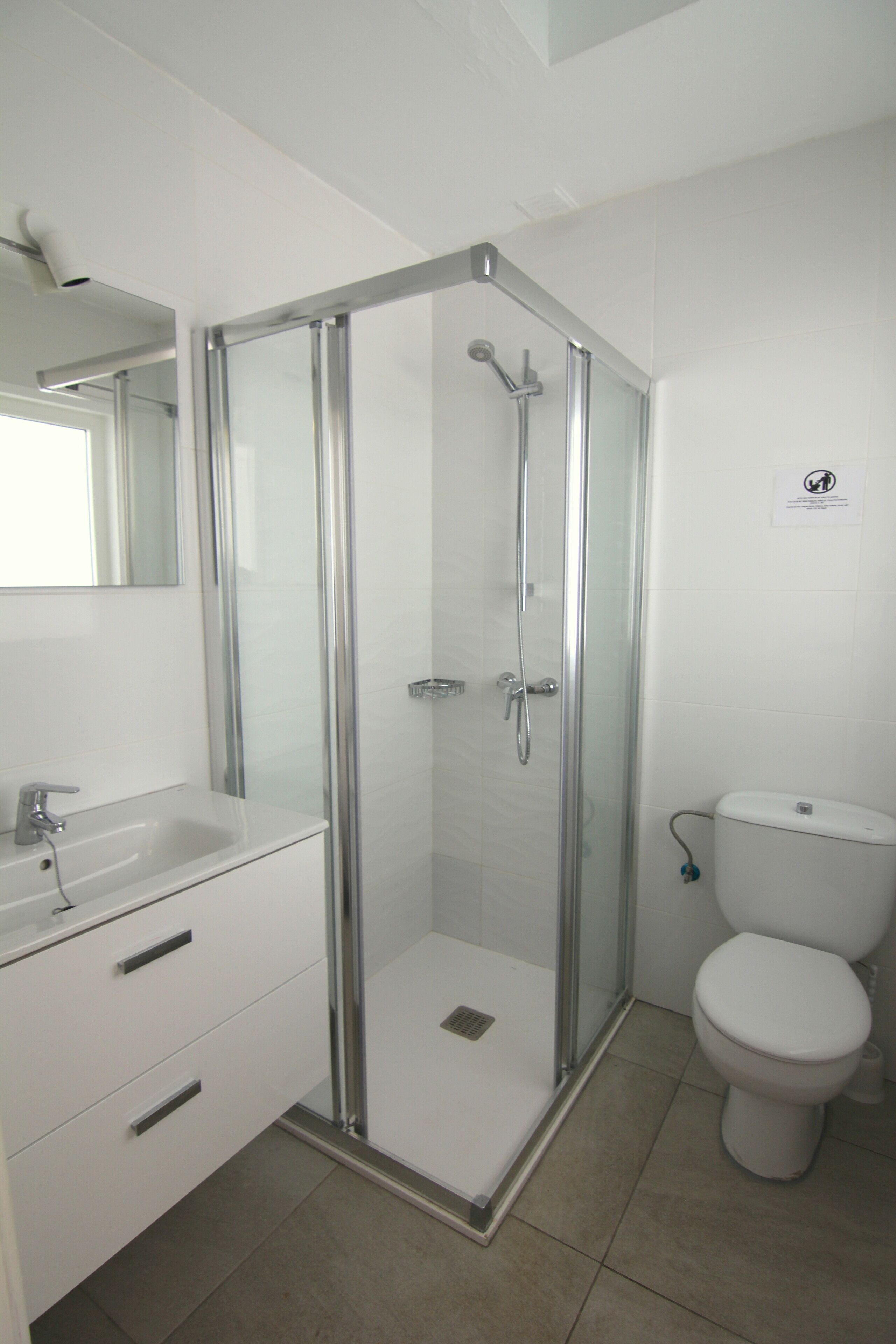 Ein modernes Badezimmer mit einer Glaskabine zur Dusche, einem weißen Waschbecken mit Spiegel und einer Toilette.