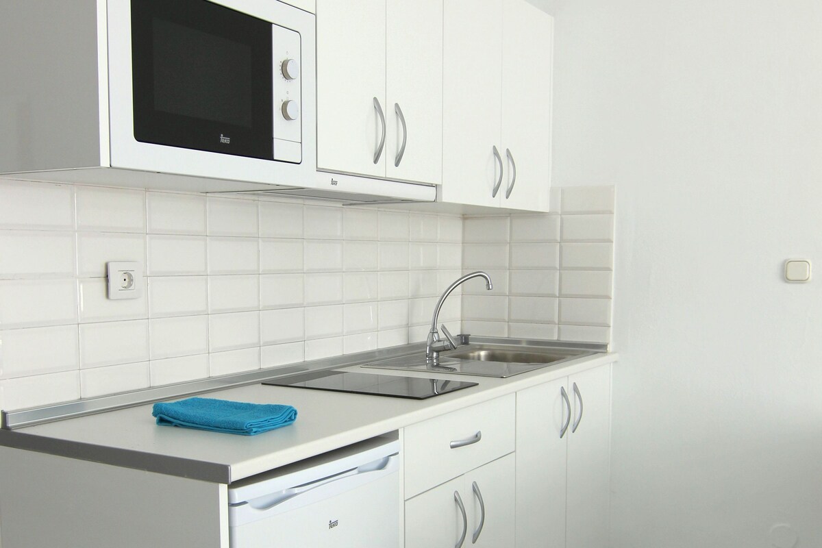A modern kitchen with white cabinetry, a built-in microwave, a sink, and a blue towel on the counter.