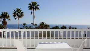 A white table and chairs on a balcony with a view of the ocean and palm trees. - Arena Dorada - Apartments (Tías)