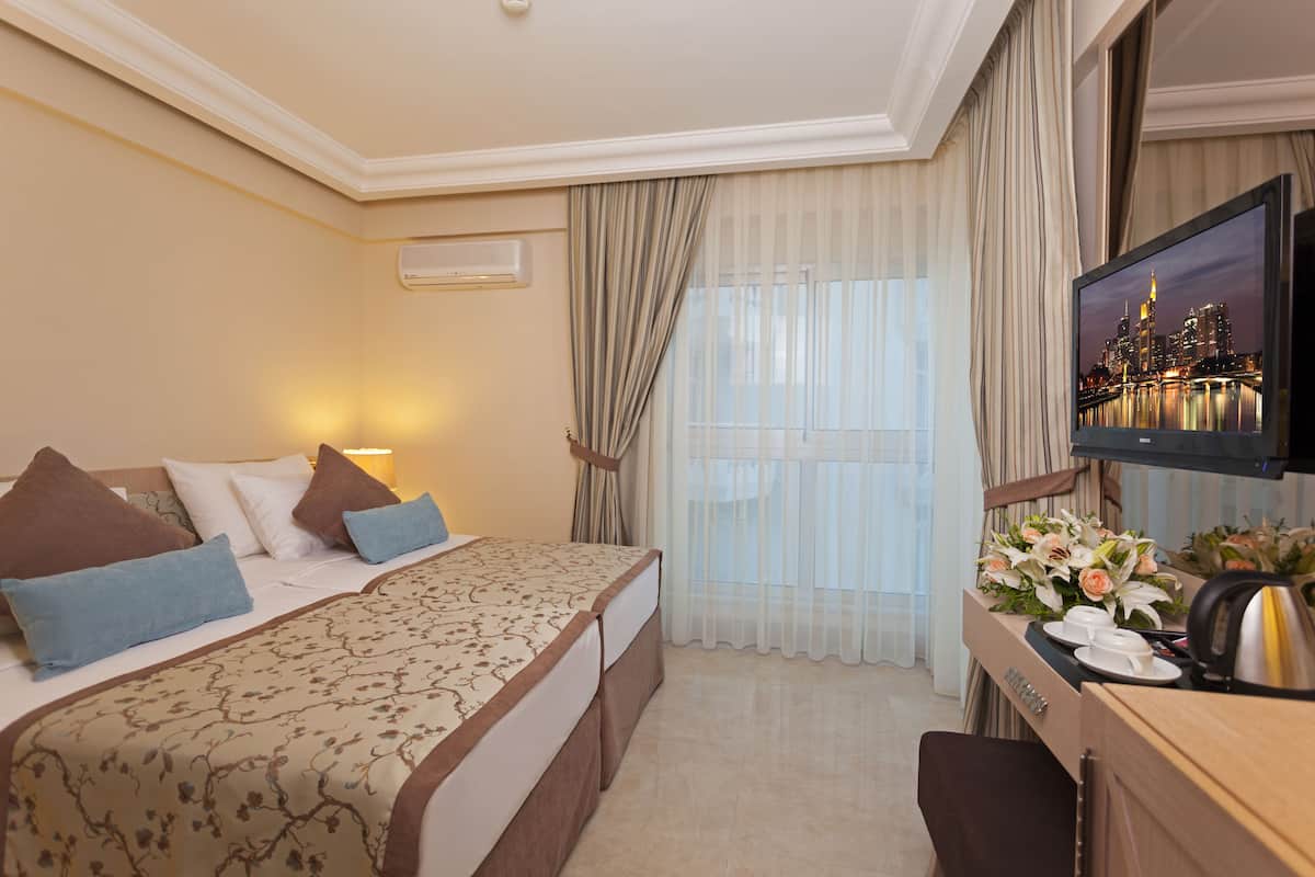 A hotel room with a bed, a desk with a telephone, and a television displaying a cityscape.