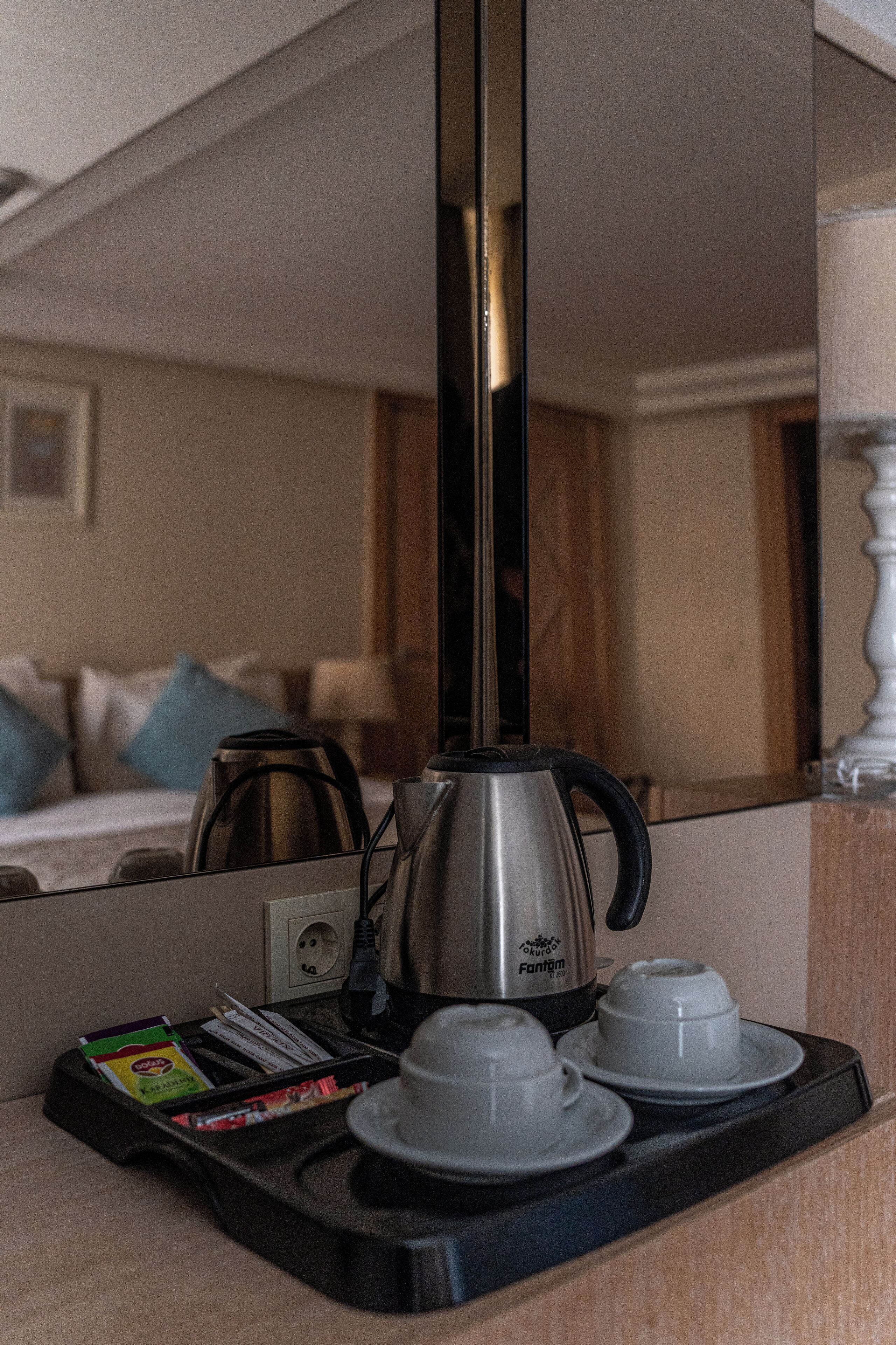 Quarto de hotel com cafeteira, duas chávenas e um tabuleiro com diversos objetos.