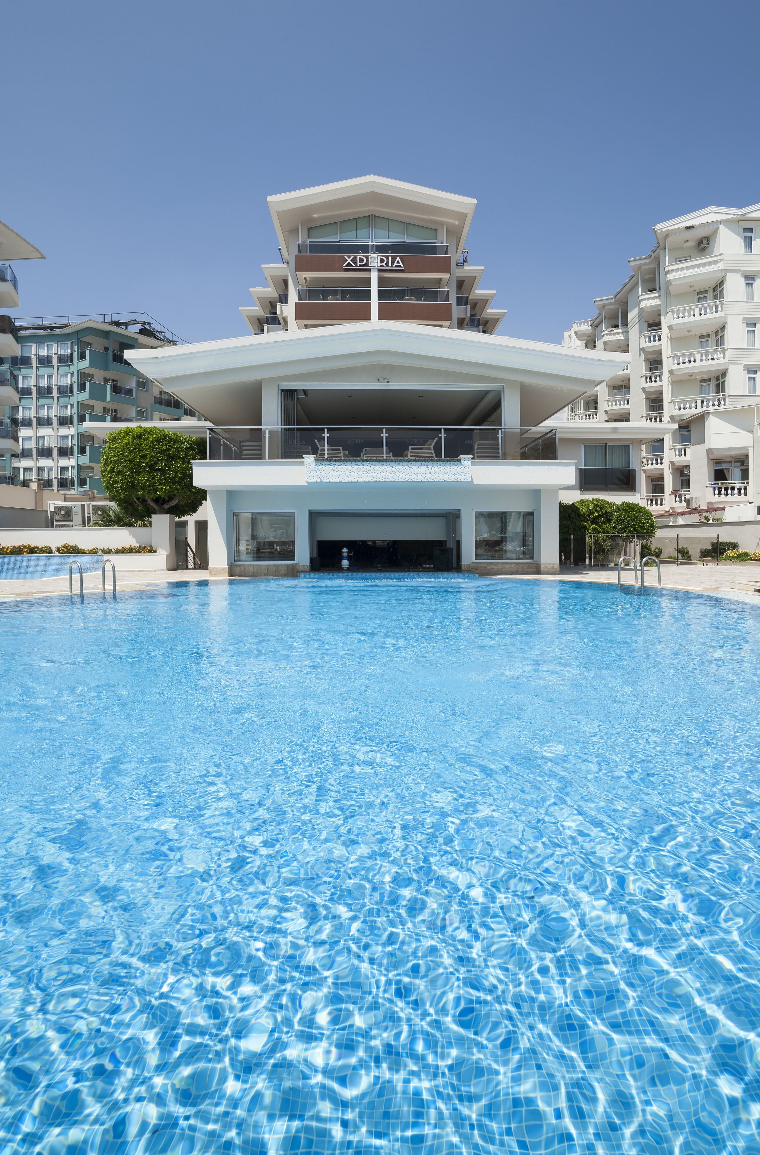 A modern hotel with a pool in front, featuring a prominent 'XPERIA' sign on the building.