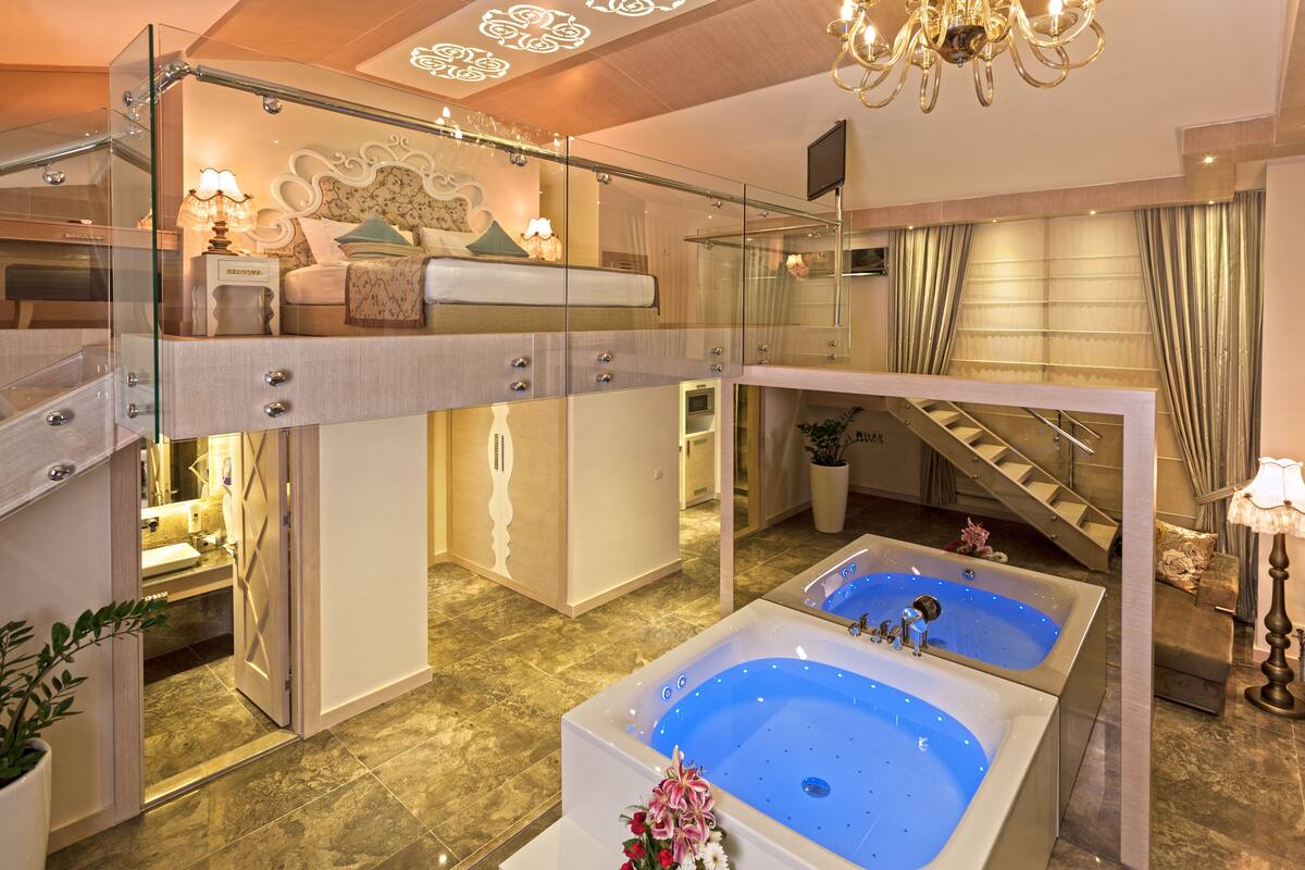 A luxurious bedroom with a glass-enclosed balcony, a large bathtub, and a modern staircase.