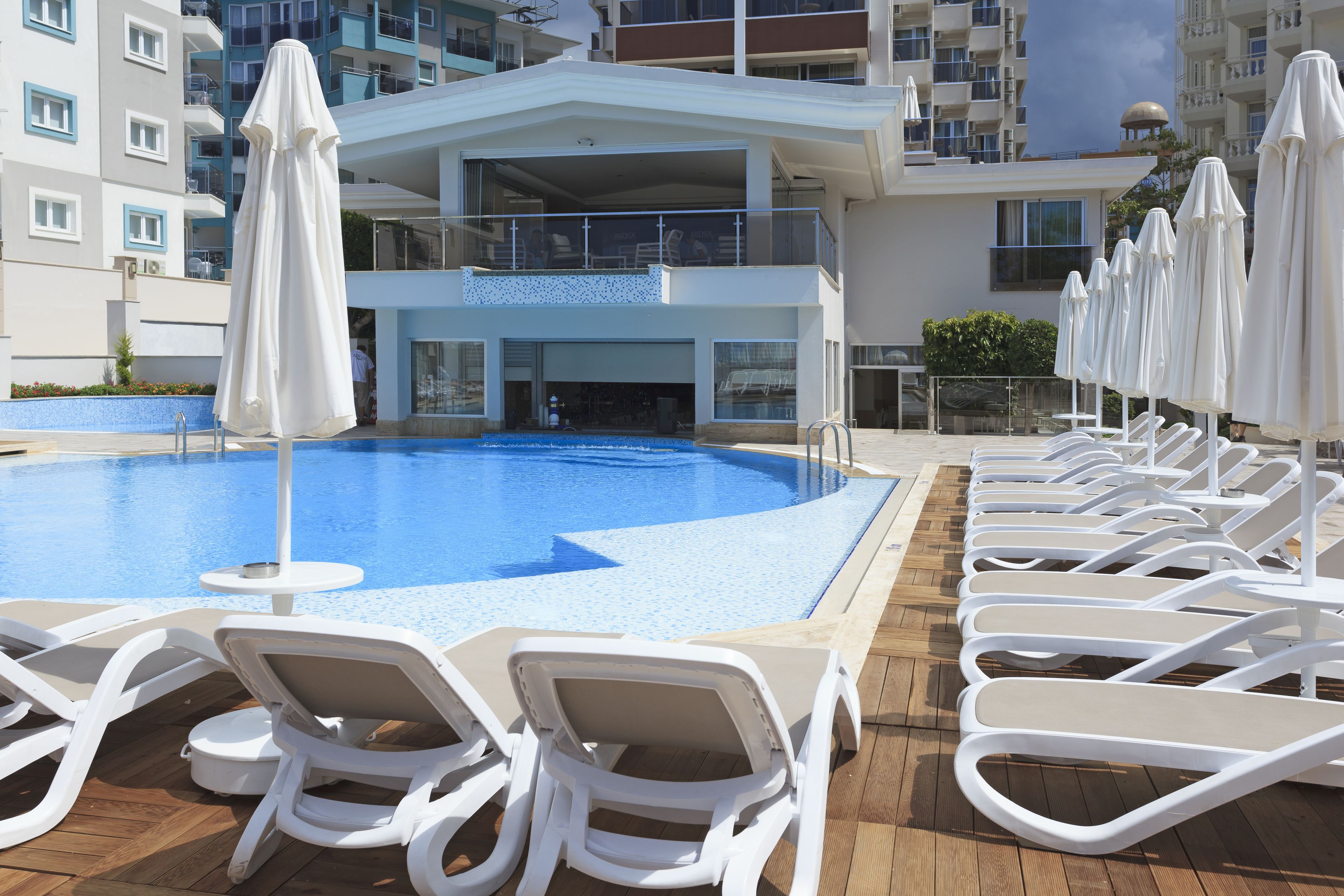A pool area with lounge chairs and umbrellas, a building with balconies, and a clear blue pool.