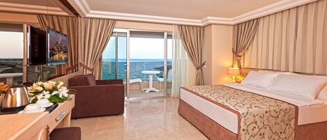 Habitación de hotel con cama, escritorio con cafetera, televisión y balcón con vista al mar.