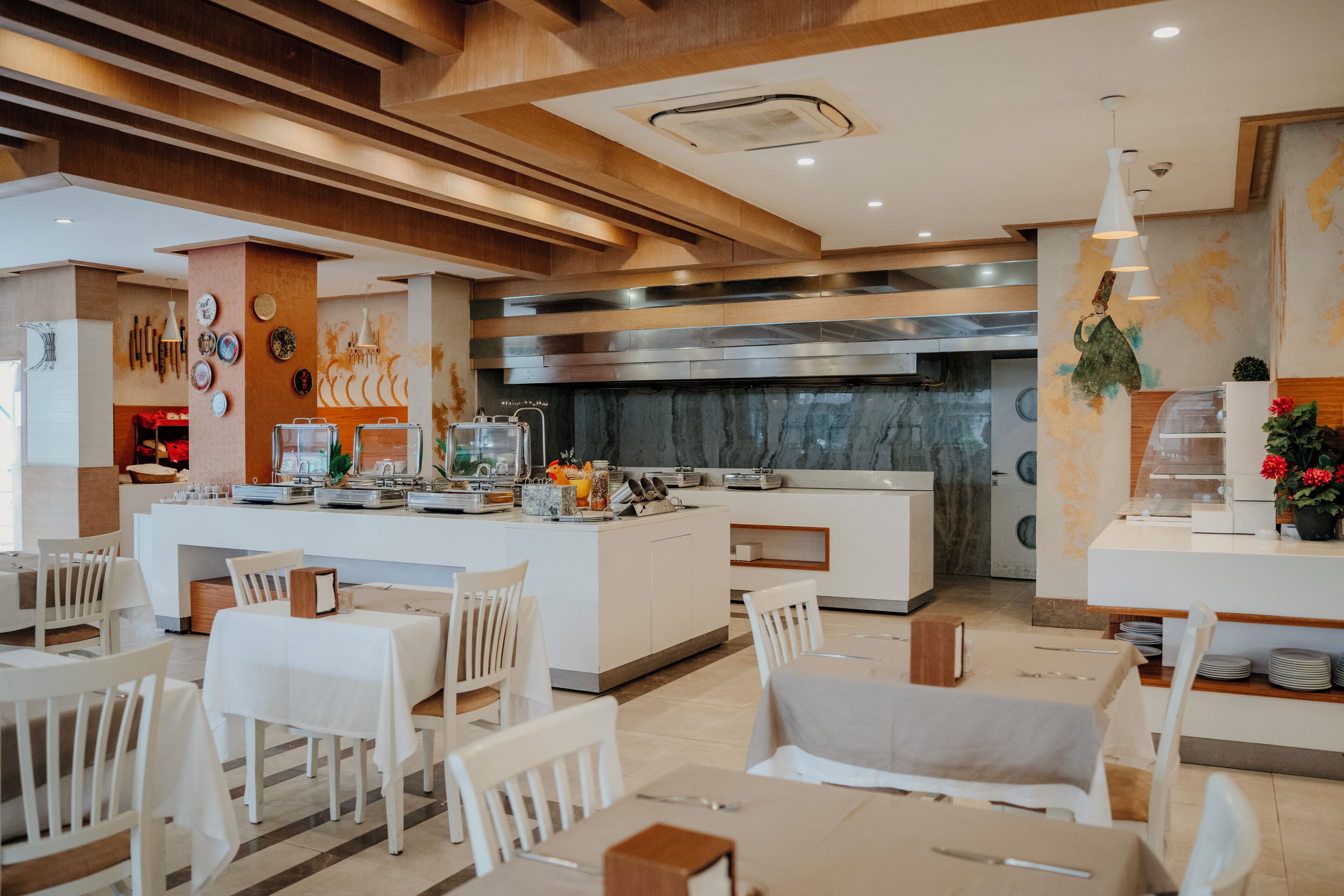 Um saguão de hotel moderno com uma ilha central, mobiliário branco e uma área de cozinha ao fundo.