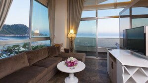 Een moderne woonkamer met een bank, een ronde tafel met bloemen, een televisie en een balkon met uitzicht op zee.