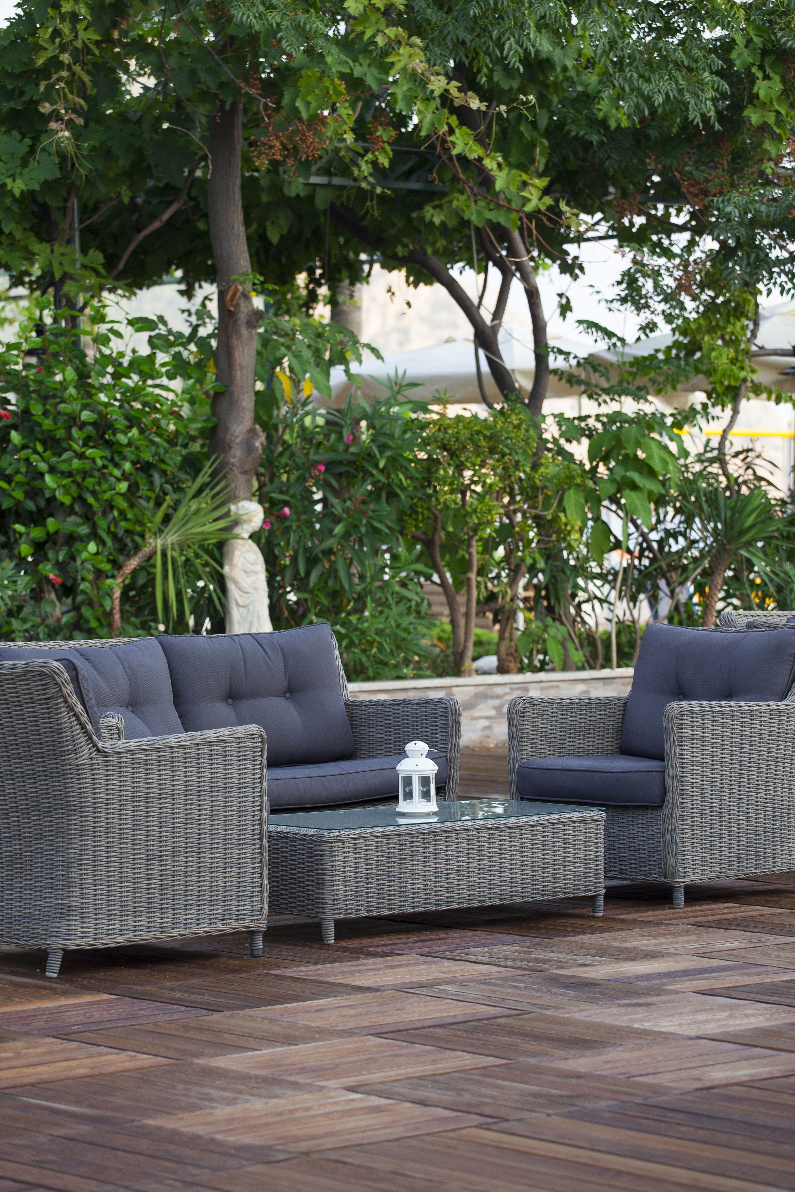 A wicker sofa set with cushions, a glass coffee table, and a lantern.