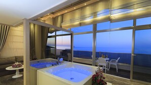 Een moderne badkamer met een ruime badkuip, een klein tafeltje met bloemen en uitzicht op de oceaan door grote ramen.