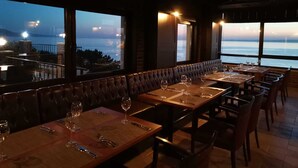 Un restaurant avec des tables dressées pour le service, une vue sur la mer et un balcon donnant sur l’eau.