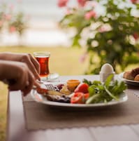 A meal with a plate of food, a glass of tea, and a cup on a table outdoors.