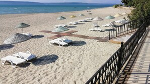 Une plage avec des chaises longues et des parasols, une promenade en bois et une rambarde le long du bord.