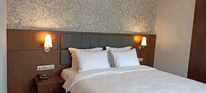 A hotel room with a large bed, two bedside lamps, a wooden nightstand with a phone, and a marble-patterned wall. - Iris Hotel & Spa (Çanakkale)