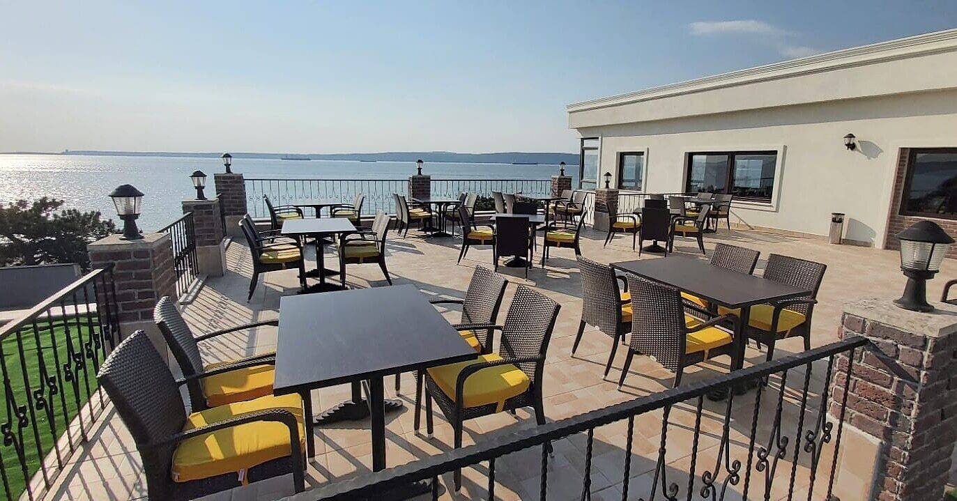 An outdoor terrace with tables and chairs, overlooking a body of water.