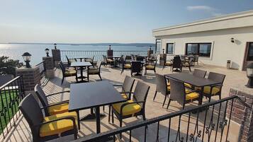 An outdoor terrace with tables and chairs, overlooking a body of water.