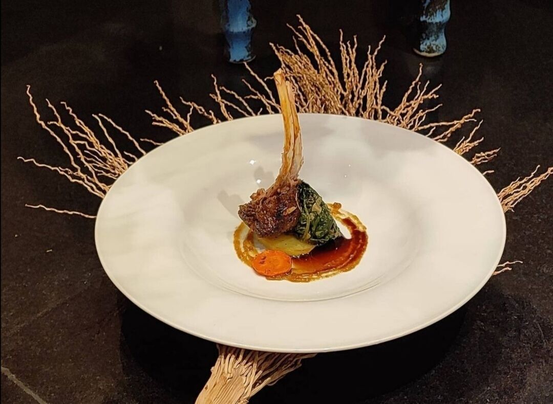 A white plate with a dish of meat, vegetables, and sauce, surrounded by decorative branches.