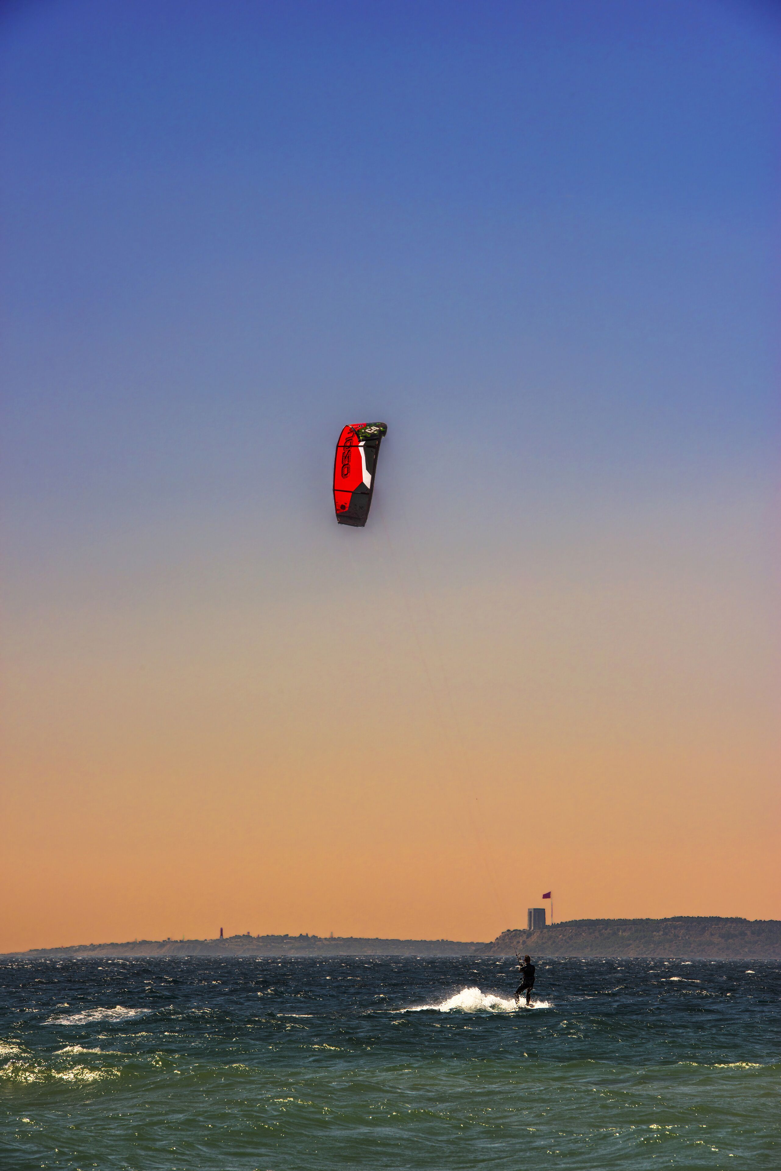 A person windsurfing with a red and black kiteboard in the ocean.