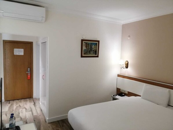 Una habitación de hotel con una cama, una mesita de noche, una lámpara de pared, un cuadro y una puerta con un letrero.