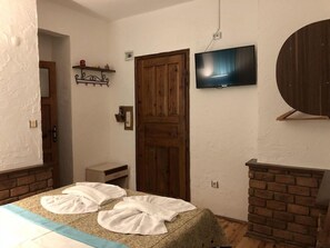 A bedroom with a bed, a television, a wooden door, and a brick fireplace. - Ozcakil Hotel (Alanya)