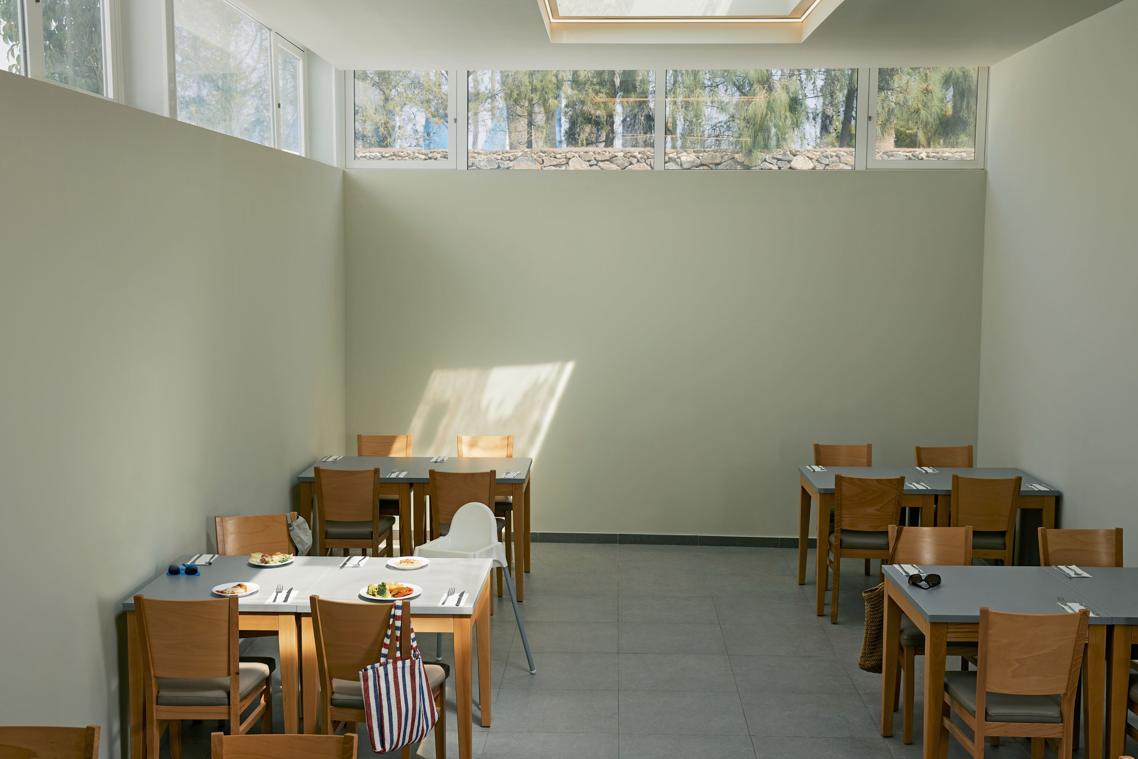 A dining area with multiple tables and chairs, large windows with a view of trees and rocks, and a skylight.