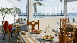 Un comedor con una mesa dispuesta para dos personas, con vista al mar y una palmera.