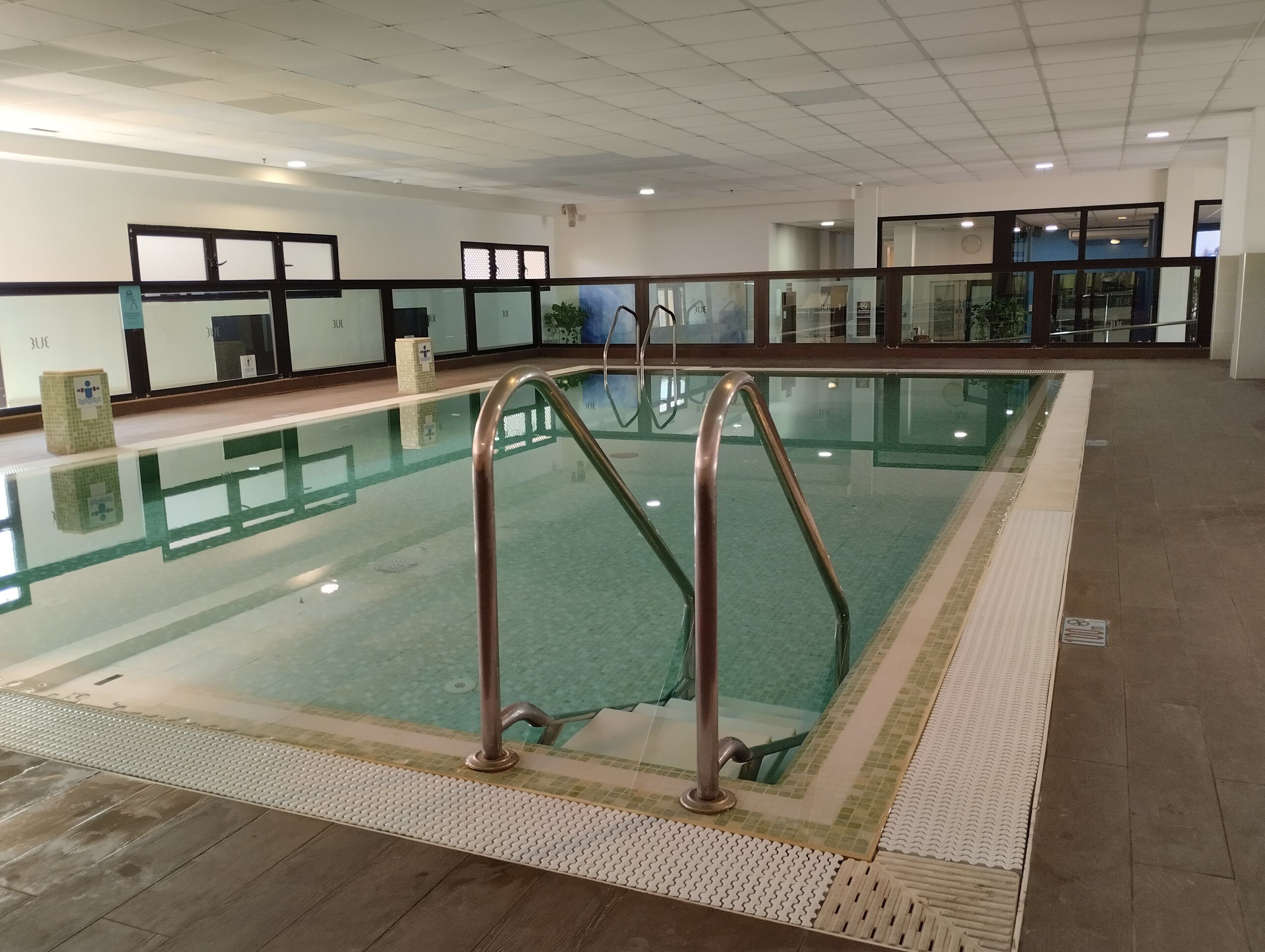 An indoor swimming pool with clear water, metal handrails, and a tiled floor.