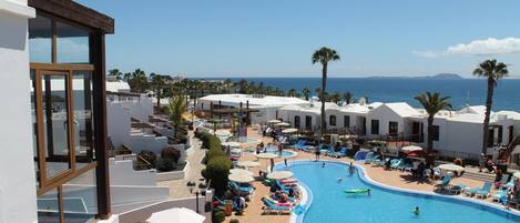Un resort con una piscina grande, tumbonas y palmeras.