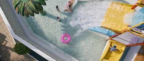Luchtbeeld van een waterpark met een golfslagbad, opblaasboten en een gele glijbaan.