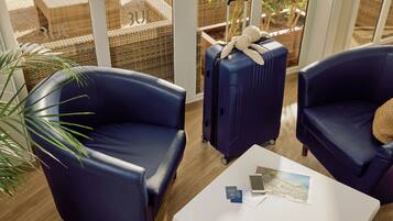 Una habitación con dos sillones azules, una mesa de centro blanca con documentos de viaje y una maleta con un peluche.