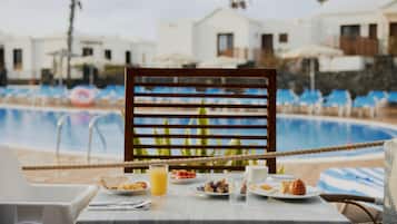 Une table à manger dressée pour le petit-déjeuner, avec vue sur une piscine et des villas.