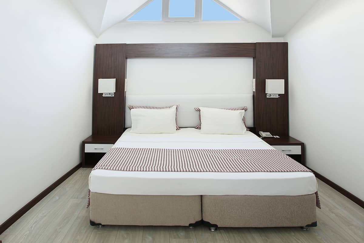 A modern bedroom with a sloped ceiling, a large bed with two pillows, bedside tables, and a small window.