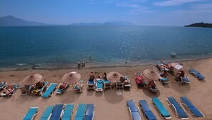 A beach with rows of sun loungers and umbrellas, a clear sky, and a distant mountain. - Arora Hotel (Kuşadası)