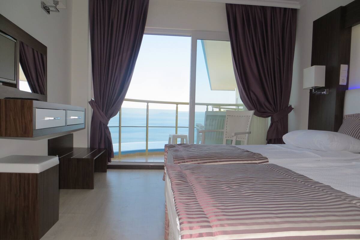 A hotel room with a bed, a desk, a chair, and a view of the sea.