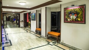 Un vestíbulo de hotel con piso de mármol, bancos de madera y obras de arte enmarcadas en las paredes.