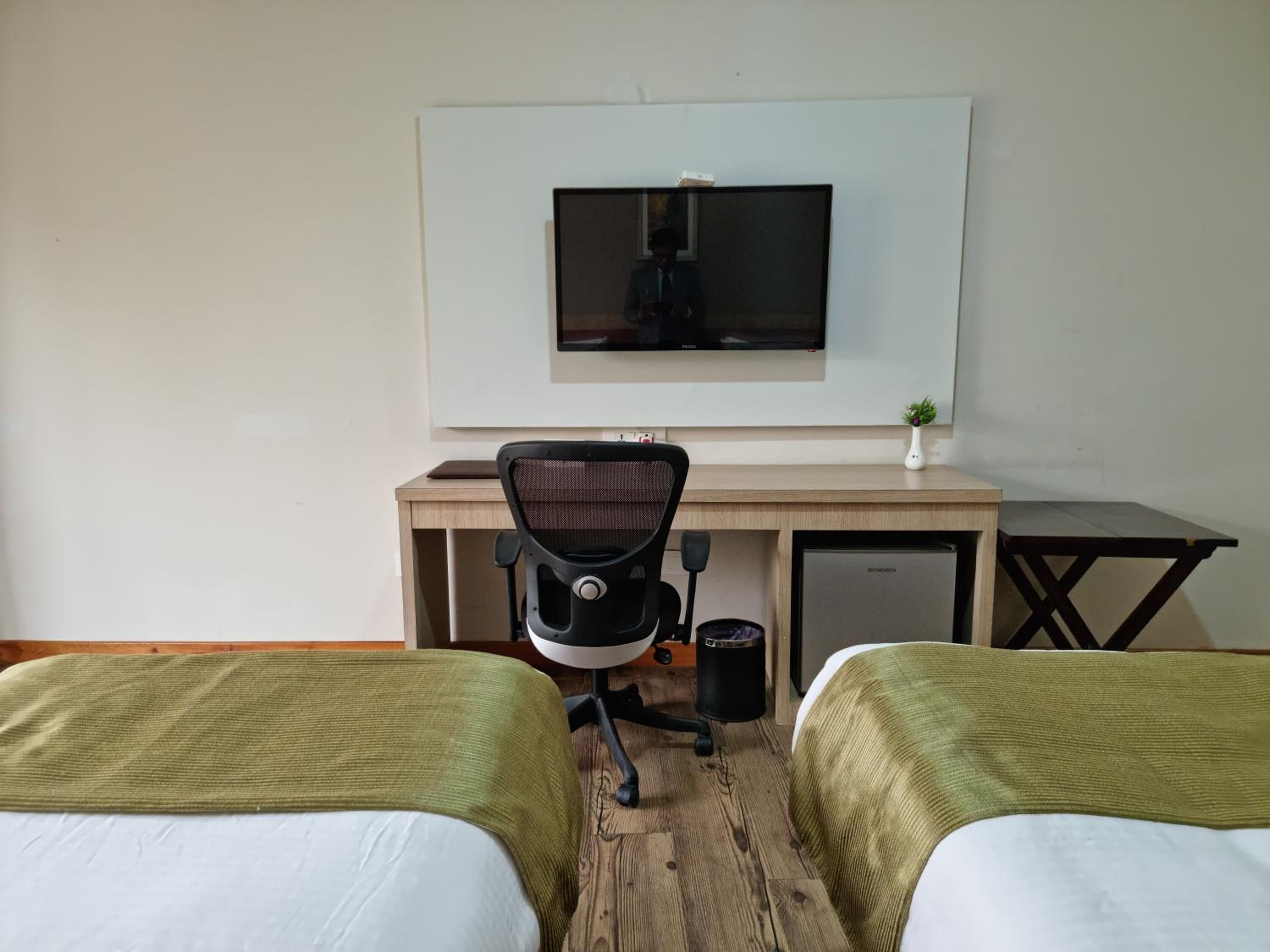 Habitación de hotel con dos camas, un escritorio con televisor, una silla, una mesita y un cubo de basura.