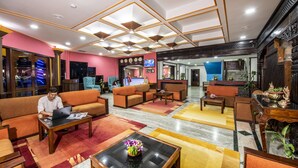 Un vestíbulo de hotel con diseño moderno, que presenta una zona de estar central con sofás y sillones, una recepción y una decoración floral.