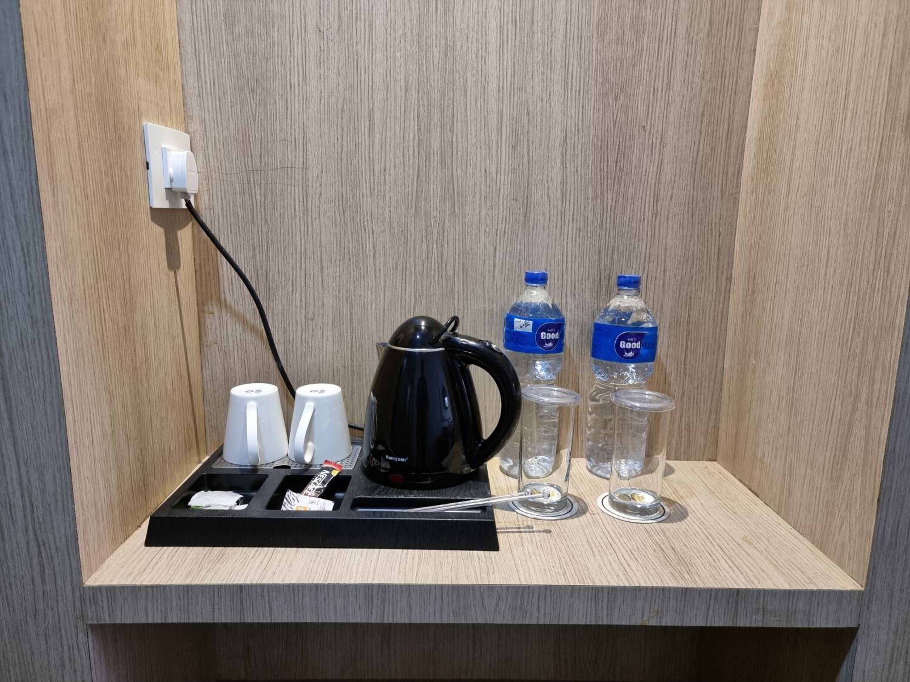 Habitación de hotel con pared de paneles de madera, una bandeja negra con tazas, una tetera y dos botellas de agua.