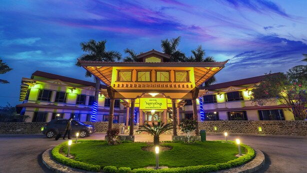 Un hotel con una entrada bien iluminada, un jardín ajardinado y un cielo despejado.