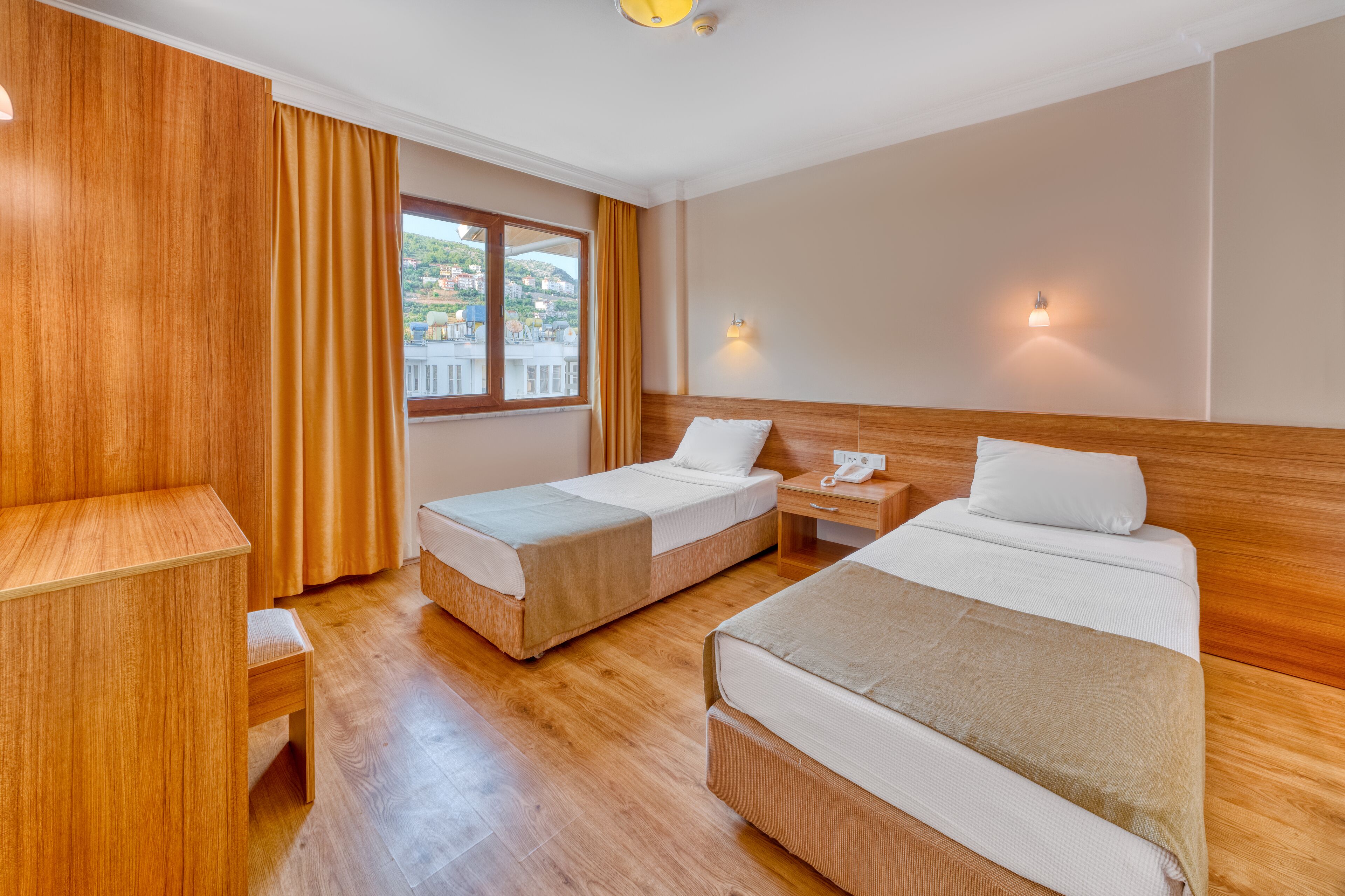 Habitació d'hotel amb dos llits individuals, un escriptori de fusta, una taula petita i una finestra amb cortines.