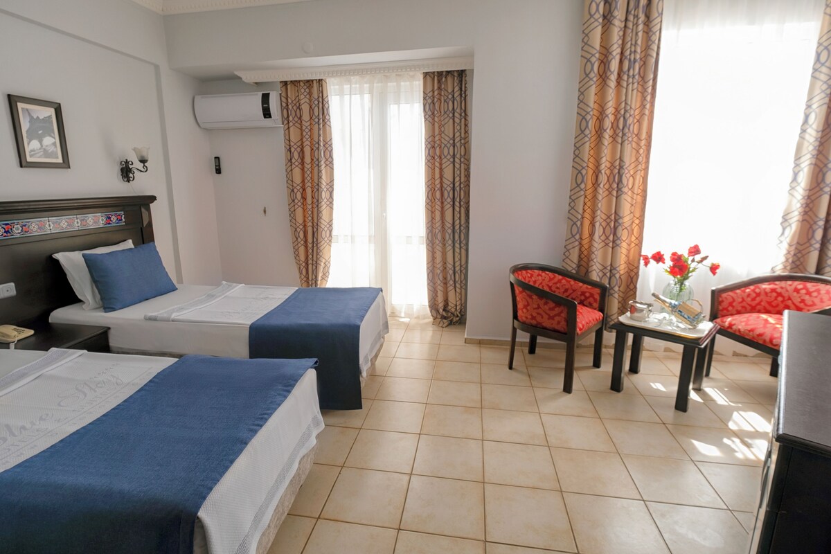 A hotel room with two beds, a small table with a vase of flowers, and a chair.