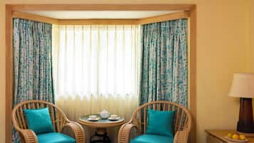 A hotel room with a bed, two wicker chairs, a small round table with a teapot and cups, and a lamp on a nightstand.